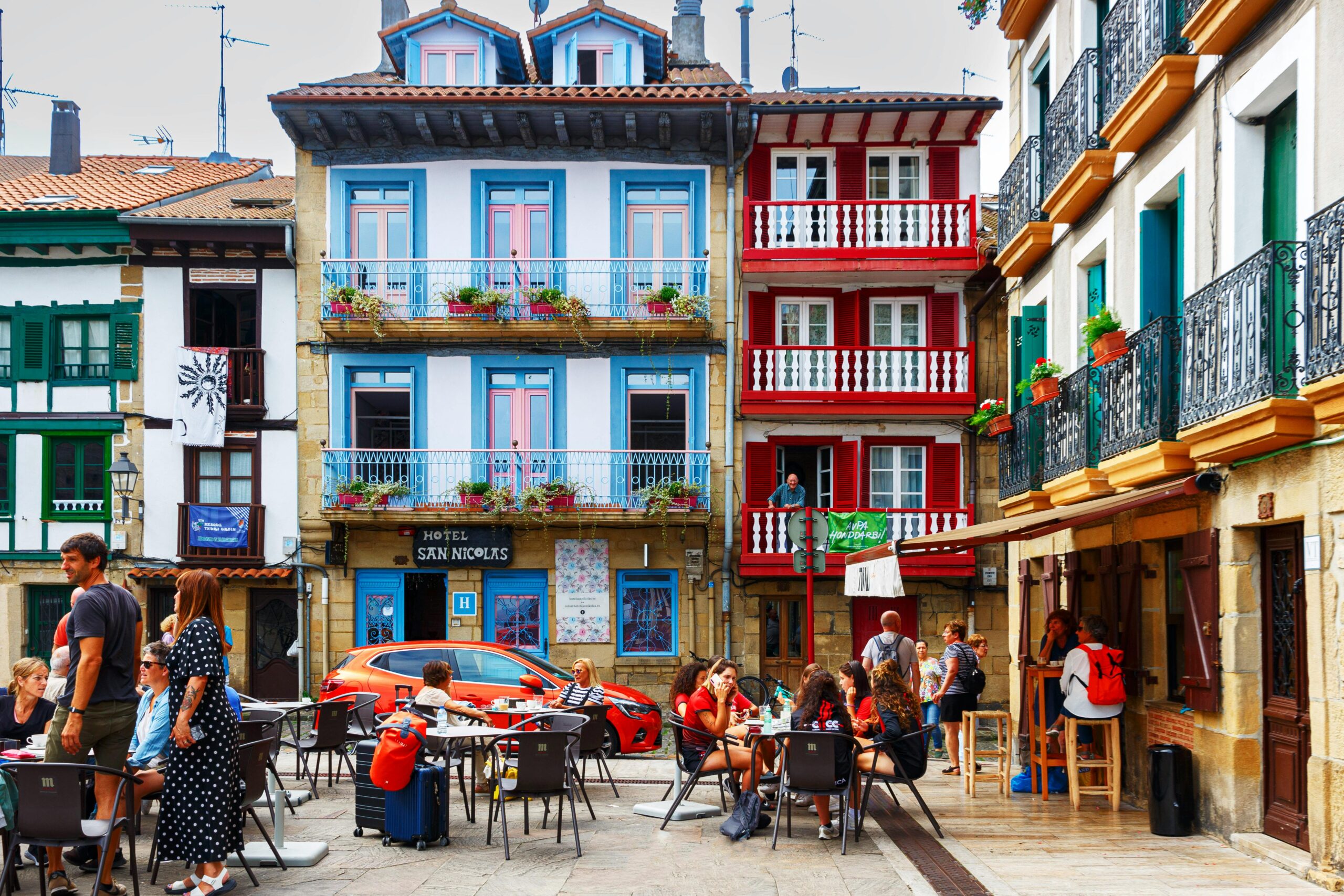 Vibrant scene of Hondarribia's historic square with colorful facades, lively cafes, and people enjoying a sunny day.