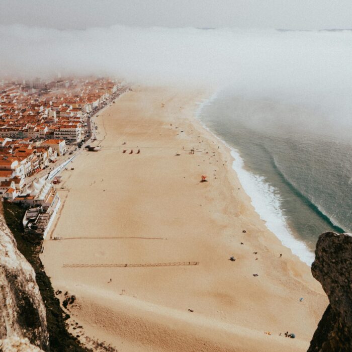 A stunning aerial view of Nazaré Beach with red roofs and fog rolling in, capturing the town's charm.