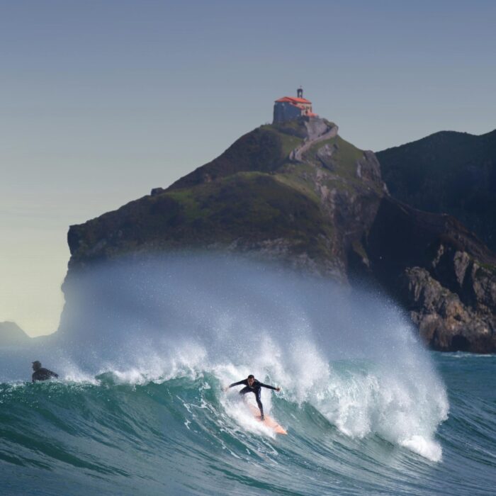 Dynamic shot of surfers catching waves by Gaztelugatxe in Basque Country, Spain.