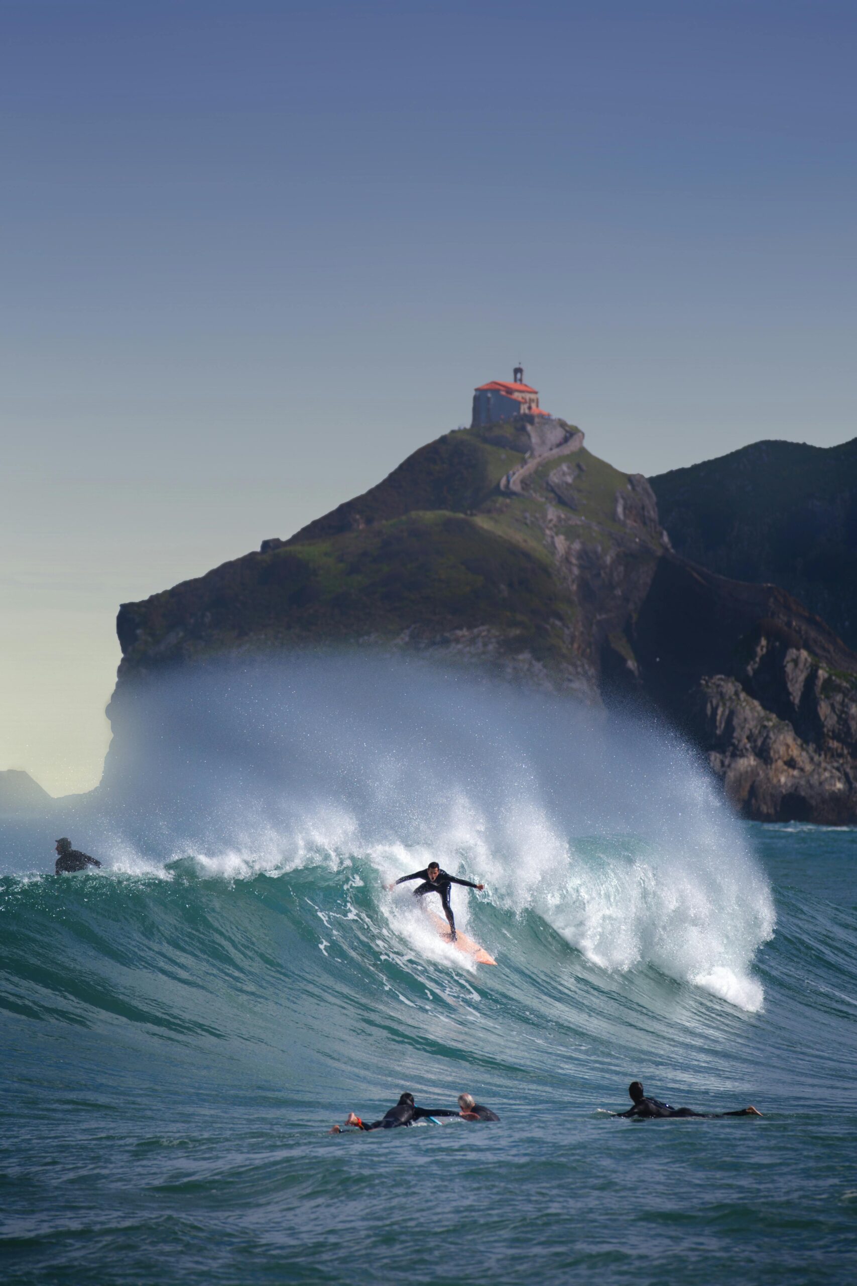 Dynamic shot of surfers catching waves by Gaztelugatxe in Basque Country, Spain.