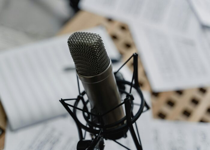 pexels-photo-6671687-6671687 Close-up of a condenser microphone on a mic stand surrounded by music sheets in a studio setting.